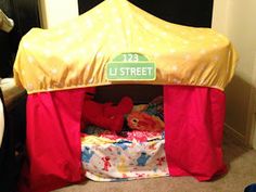 a tent that is sitting on the floor next to a bed with a red and yellow cover over it