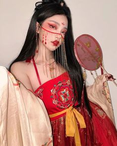 a woman dressed in red holding a mirror with chains attached to her face and wearing an elaborate head piece