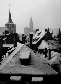 black and white photograph of rooftops covered in snow with church steeple in the background