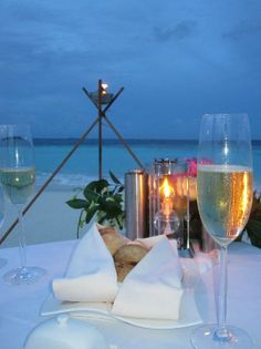 two glasses of wine are sitting on a table with food and drinks in front of the ocean