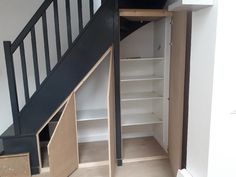 an open closet under the stairs in a room with white walls and black railings