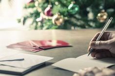 a person writing on a piece of paper with a pen in their hand, next to a christmas tree