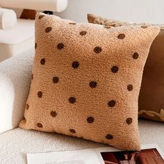 a brown pillow sitting on top of a white couch next to a book and chair