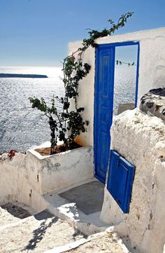 an open blue door on the side of a white building with water in the background