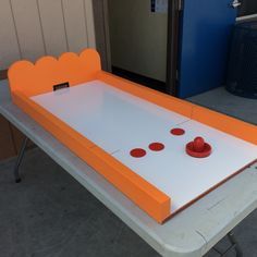 an orange and white table with three red cups on it's top, sitting in front of a blue door