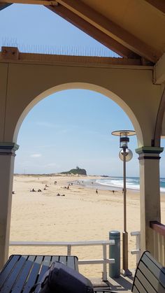 an archway on the side of a beach with people in the water and sand behind it