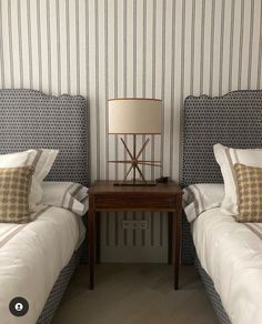 two twin beds with white sheets and pillows next to a lamp on a small table