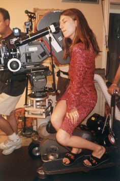 a woman sitting on top of a chair in front of a movie camera while another man stands behind her