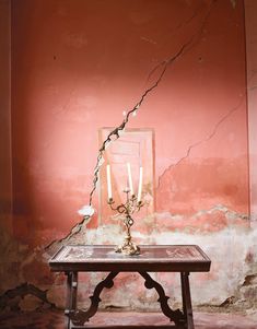 a table with a candle on it in front of a wall that has peeling paint