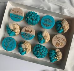 twelve cupcakes in a white box with blue frosting and designs on them