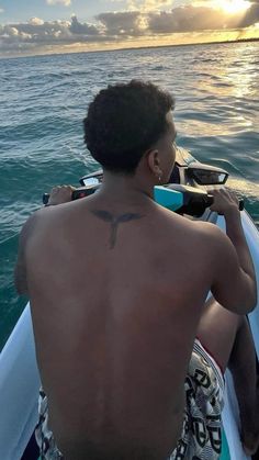 a man with a cross tattoo on his back sitting in a boat at the ocean