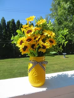 a yellow mason jar filled with sunflowers on top of a white table outside