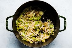 a pot filled with vegetables on top of a white countertop next to a wooden spoon