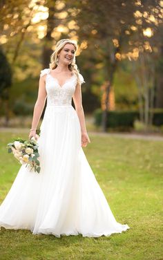 a woman in a wedding dress holding a bouquet and smiling at the camera while standing on grass