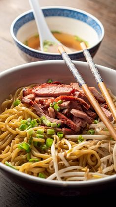 two bowls filled with noodles and meat next to chopsticks on a wooden table