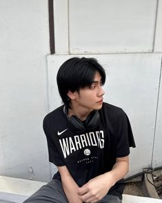 a young man with black hair sitting on a bench