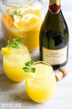 two glasses filled with lemonade next to a bottle of champagne