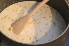 a wooden spoon in a pot filled with milk and corn on the cob kernels