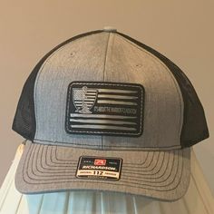 A Gray And Black Richardson Original 112 Trucker Adjustable Hat. Emblem Reads "It's About The Warrior Foundation. New. From Smoke Free Home Gray Trucker Hat For Sports, Richardson 112 Hats, Yellow Baseball Cap, Nba Caps, Black Warrior, Uss Lexington, Camouflage Hat, Usa Baseball, Adjustable Black Military Trucker Hat