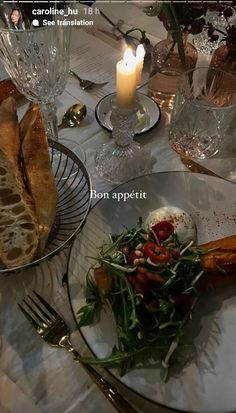 there is a plate with bread and salad on it next to a glass candle holder