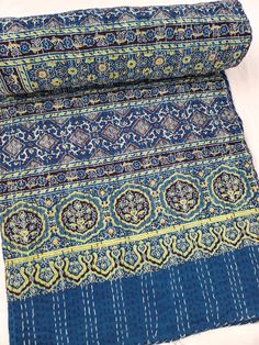 a blue and yellow area rug laying on top of a white bed sheet with an intricate design