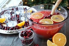 a glass bowl filled with cranberry punch surrounded by orange slices and cranberries