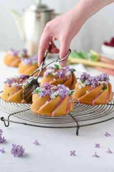 a person is cutting into some cake on a wire rack with purple flowers around it