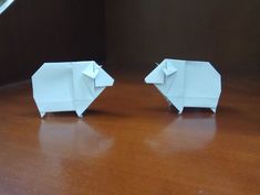 two white origami elephants sitting on top of a wooden table next to each other