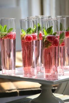 four glasses filled with water and raspberries on top of a table next to each other