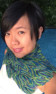 a woman wearing a green and blue knitted scarf on top of a table next to a pool