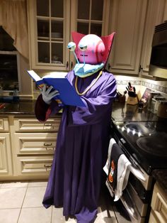 a costumed person standing in a kitchen reading a book