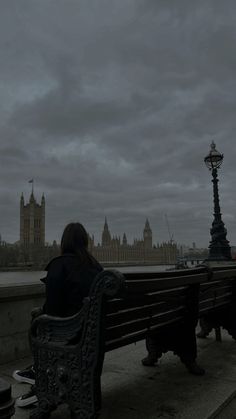 a person sitting on a bench in front of the big ben clock tower and houses of parliament