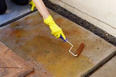 a person in yellow gloves painting concrete with a paint roller