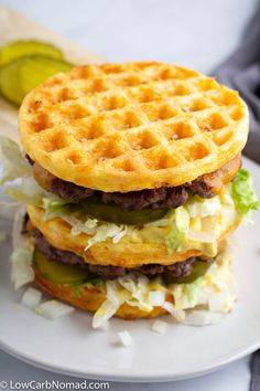 a stack of waffle sandwiches on a white plate with pickle slices in the background