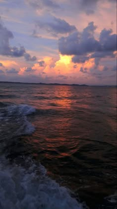 the sun is setting over the ocean with waves coming in to shore and clouds above