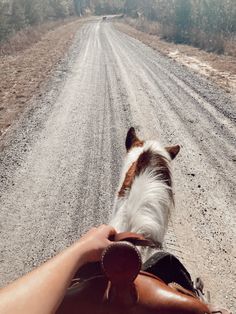 a person riding on the back of a brown and white horse down a dirt road