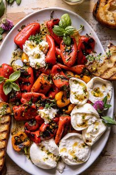 a white plate topped with tomatoes, mozzarella and other toppings next to bread