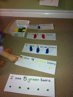 a child is sitting on the floor and playing with cut out paper animals that read i see 5 green bears