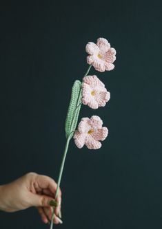 crocheted pink flowers being held by a person's hand on a black background