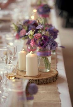 the table is set with candles and flowers in mason jar vases on wood slices