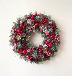 a christmas wreath hanging on the wall with pine cones, berries and evergreens around it