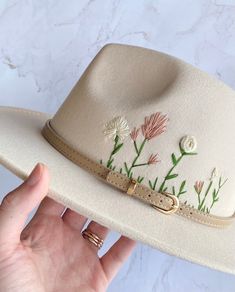 a woman's hand holding a white hat with flowers on it