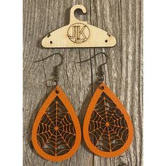 wooden earrings with spider web on them and an orange tear shaped earring hanging from a hook