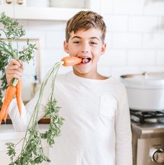 a young boy holding carrots in his hands and sticking them out to eat it