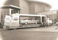 an old photo of a car being loaded onto a truck by a man standing in front of a building