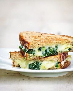 two grilled sandwiches on a white plate with cheese and spinach in the middle