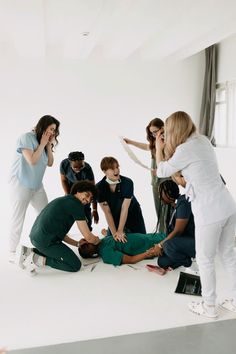 a group of people standing around each other in front of a white wall with one person on the ground