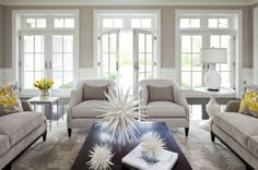 a living room with couches and chairs in front of two large windows, one has yellow flowers on the coffee table