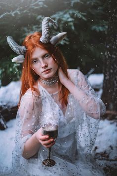 a woman with horns holding a drink in her hand and posing for the camera while wearing a white dress