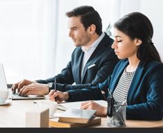 two people sitting at a table working on laptops